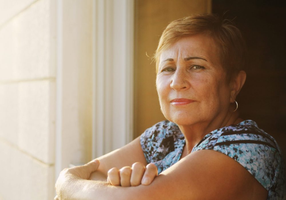 older latina woman looking out from her balcony