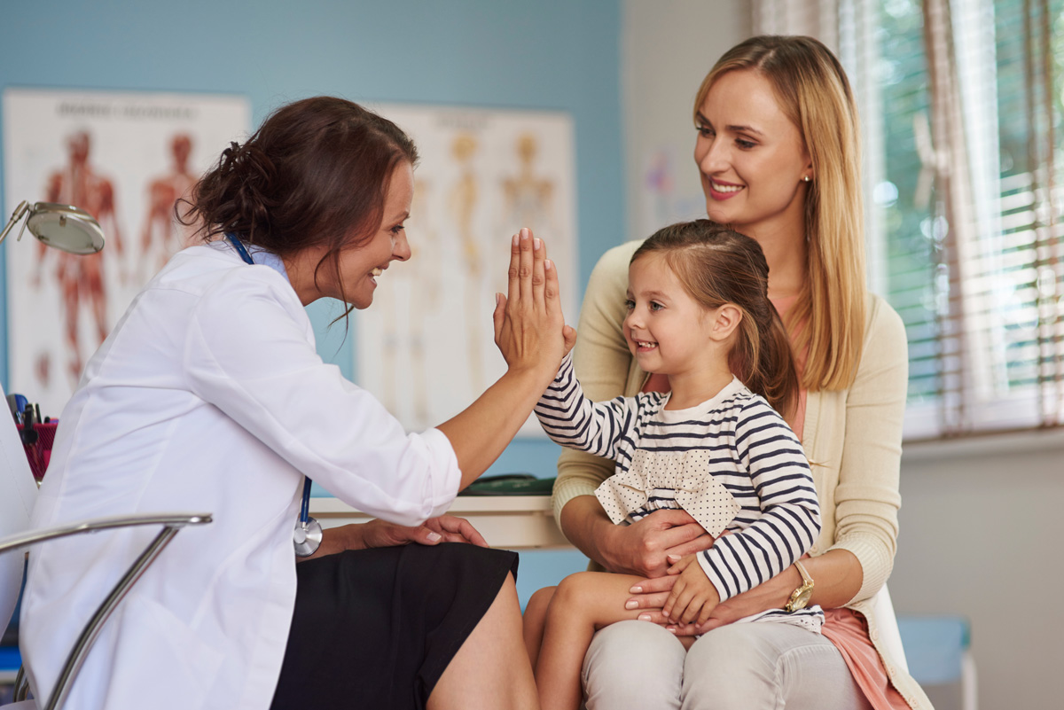 A small girl sitting on her mother’s lap while high-fiving a family physician in El Paso.