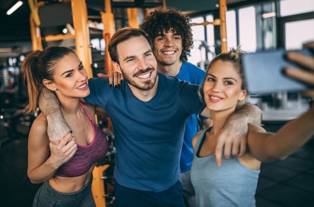 Four young adults smiling and taking a selfie at the gym after working out